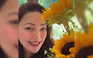 Woman smiling beside a bouquet of bright yellow sunflowers outdoors.
