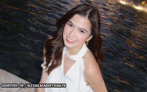 Young woman with dark hair in a white sleeveless top smiling beside a body of water.