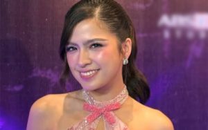 Smiling woman in a pink beaded halter-neck dress at a formal event, purple backdrop behind her.