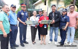 A group of uniformed officers and civilians posing outdoors while presenting ceremonial plaques to three women in the center.