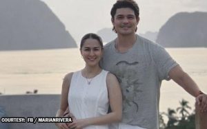Smiling couple standing on a sandy beach with cliffs in the background, posing for a photo.