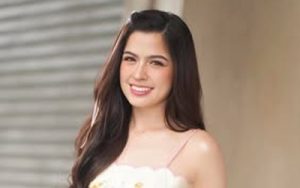 Smiling woman with long dark hair wearing a light floral top, standing outdoors.